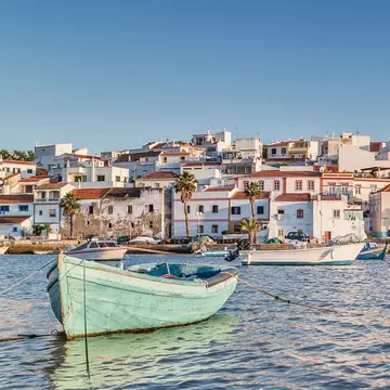 Small fishing boats moored in a harbor near a small seaside town of white buildings with red roofs.