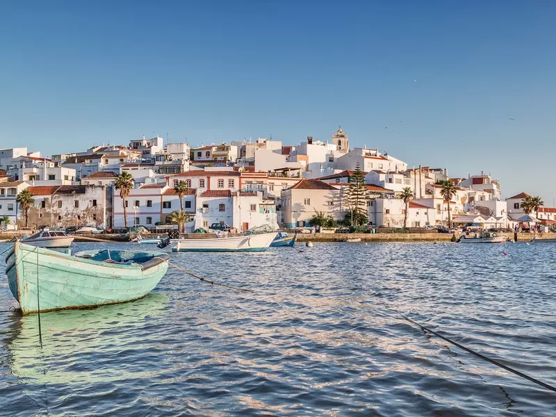 Small fishing boats moored in a harbor near a small seaside town of white buildings with red roofs.