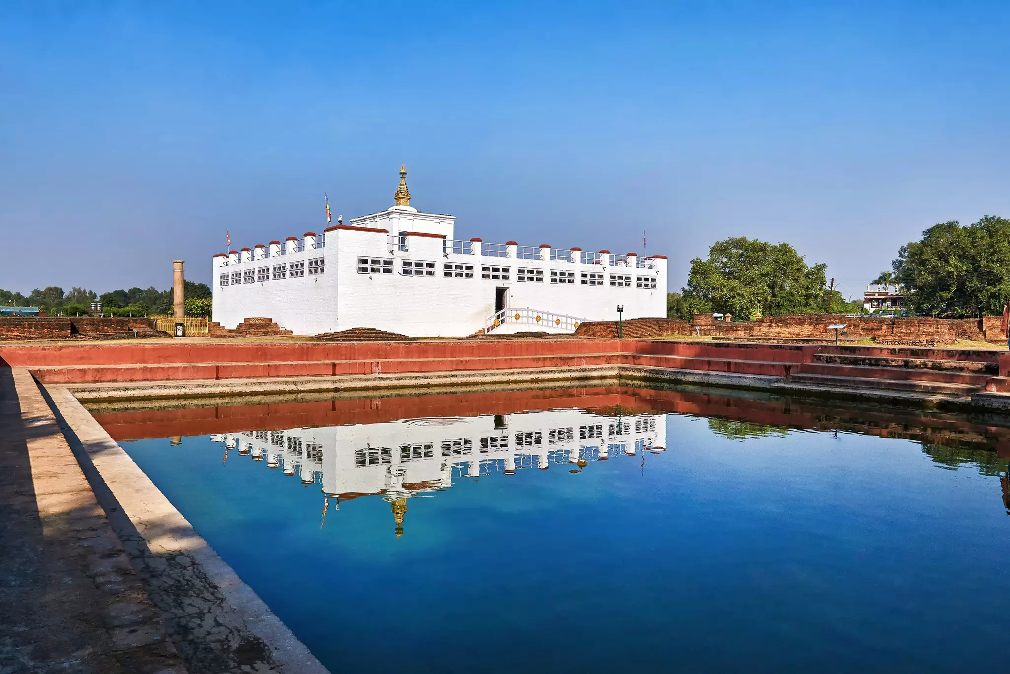 A white rectangular temple building reflected in a nearby pond.