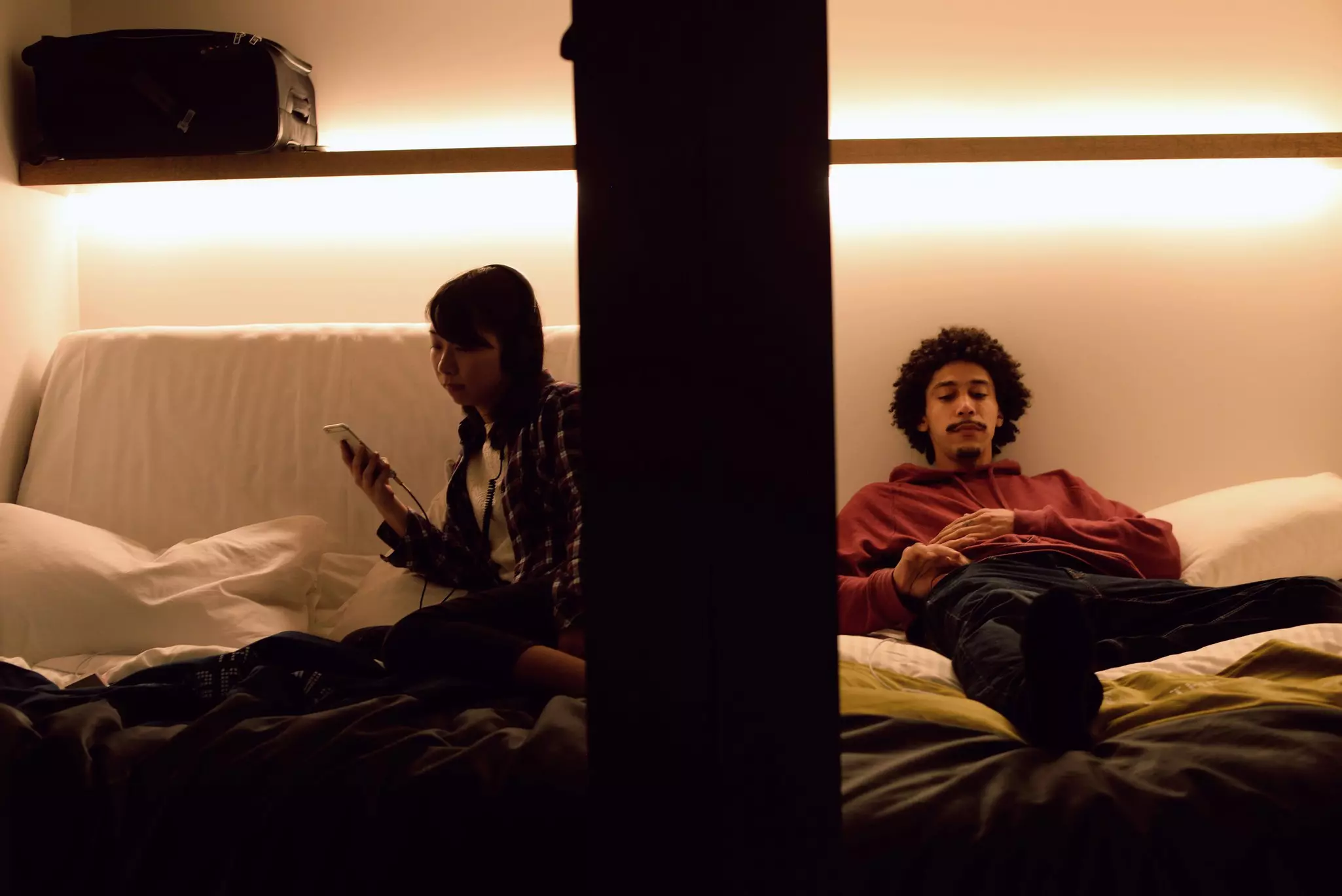 Two people in adjacent pod compartments in a capsule hotel in Japan. 