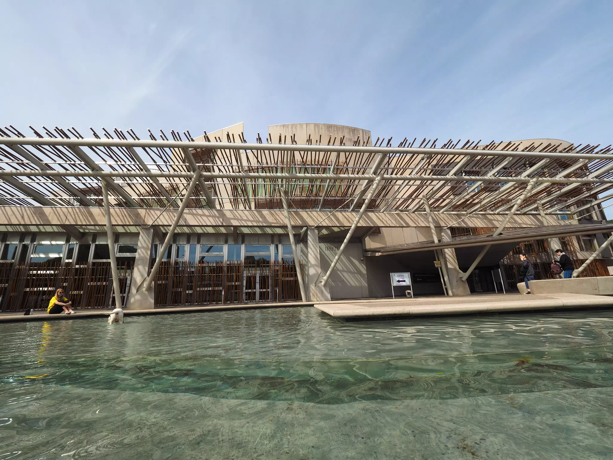 A woman sits by a pool at the Scottish Parliament while her dogs plays in the water