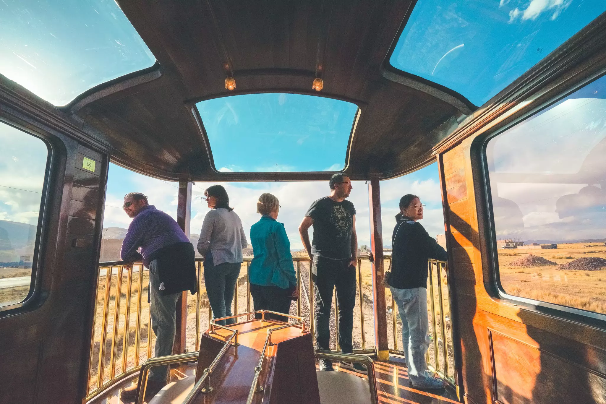 People stand in the last car of a train observing the passing desert landscape.