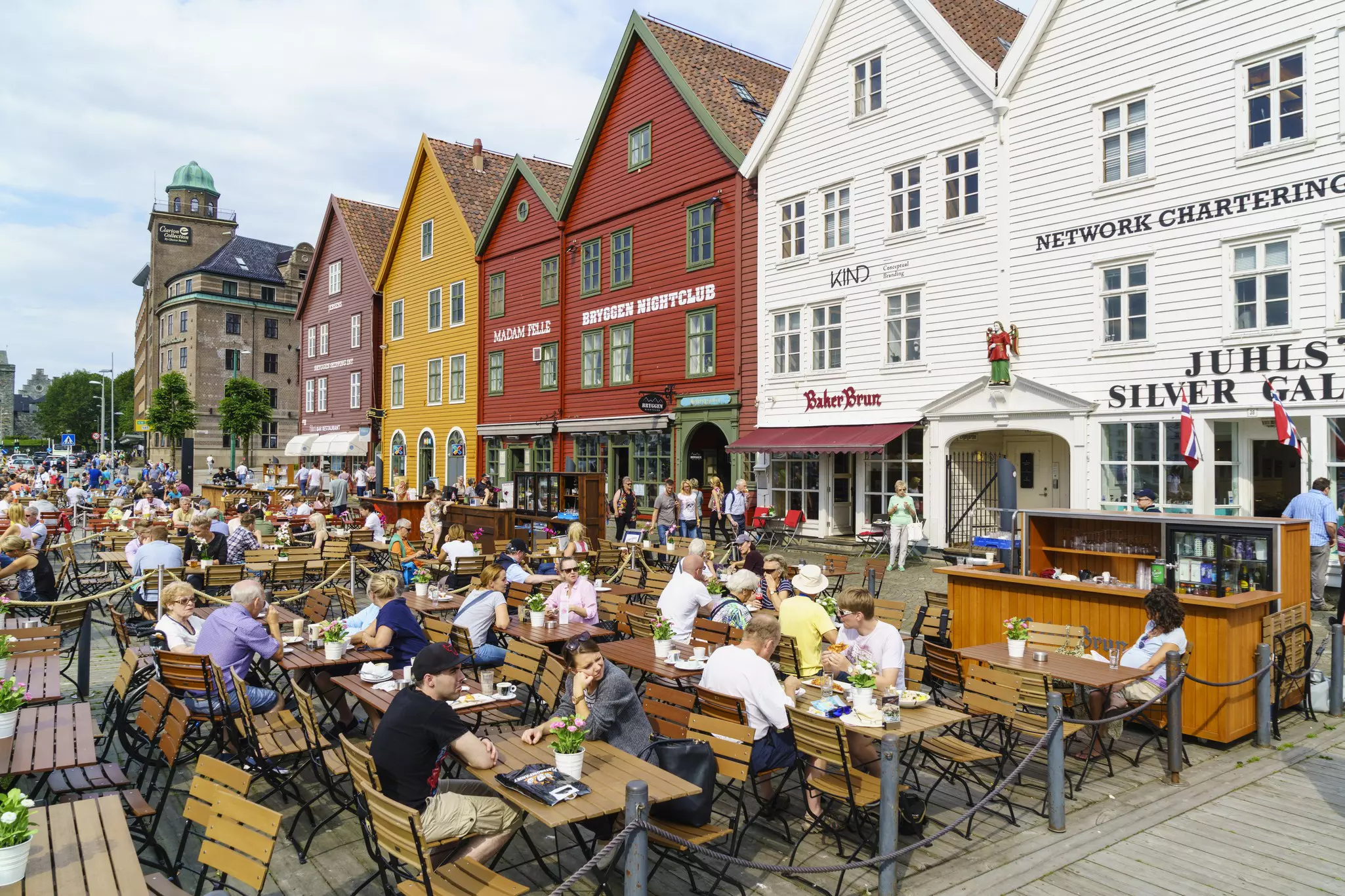 People sit at outdoor cafes in front of historic, brightly painted buildings in a city.