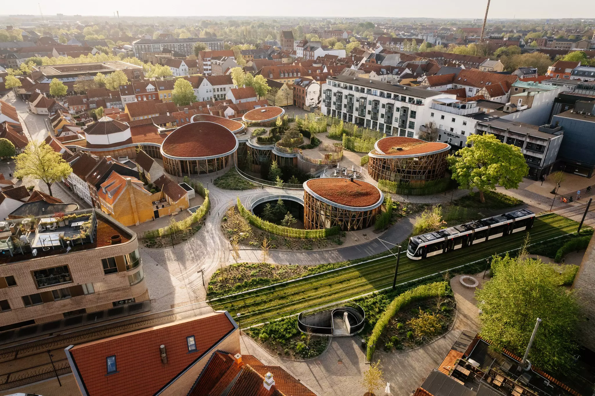 An overhead view of a museum with gardens and numerous pavilions in a city. A tram passes the museum, while apartment buildings surround the complex.