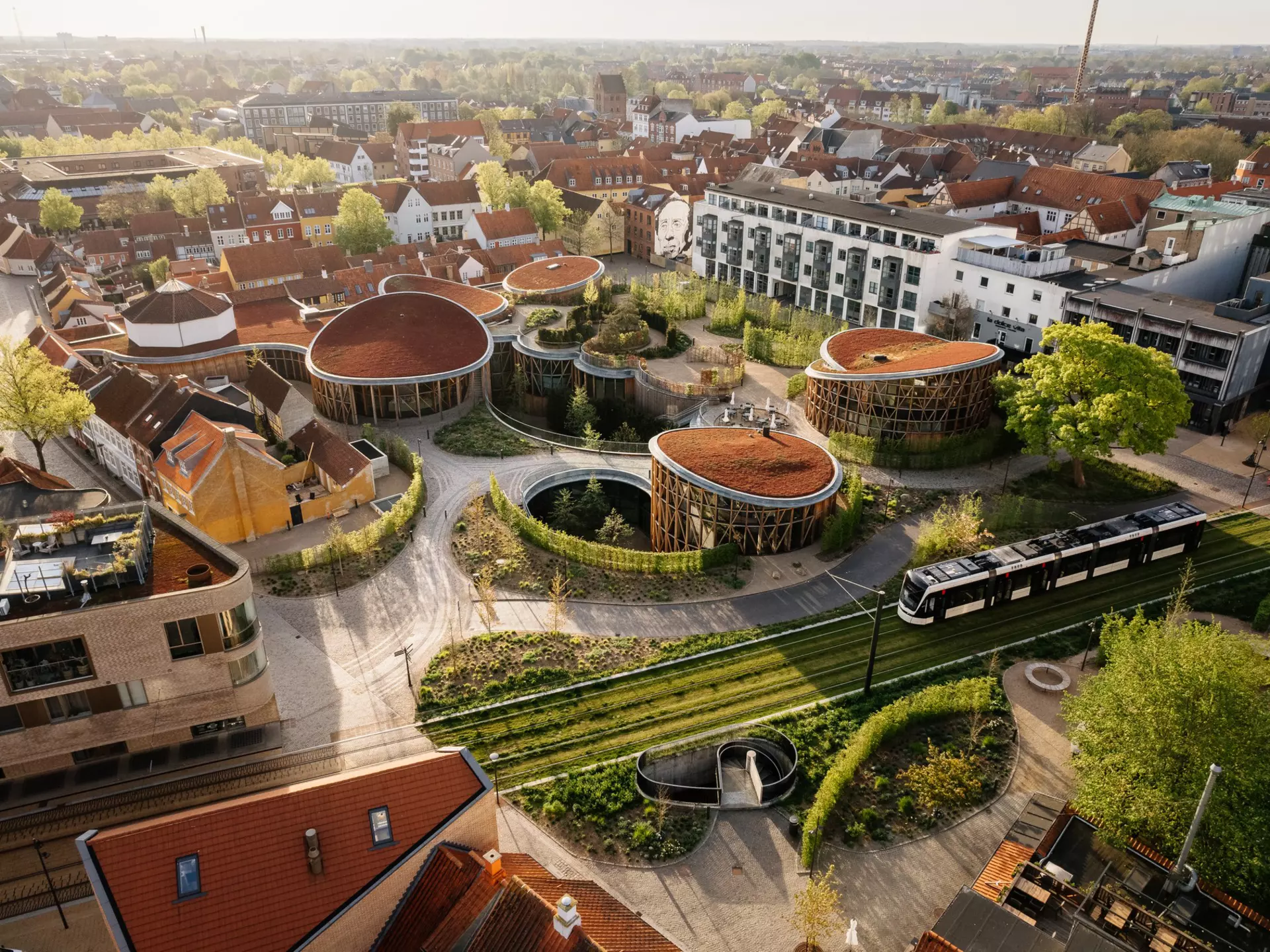 An overhead view of a museum with gardens and numerous pavilions in a city. A tram passes the museum, while apartment buildings surround the complex.
