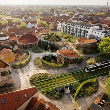 An overhead view of a museum with gardens and numerous pavilions in a city. A tram passes the museum, while apartment buildings surround the complex.