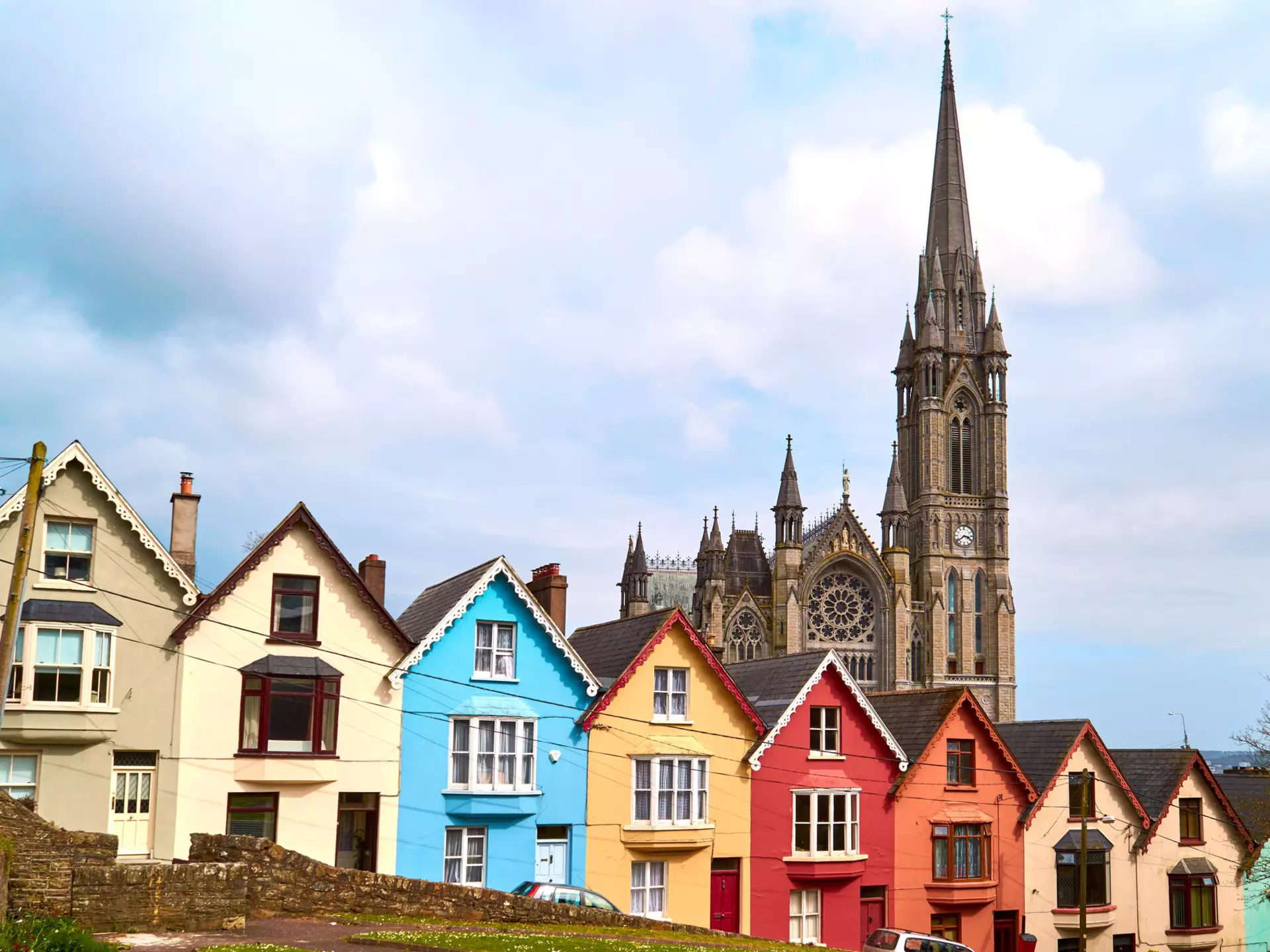 A stone cathedral is behind a row of brightly colored houses.