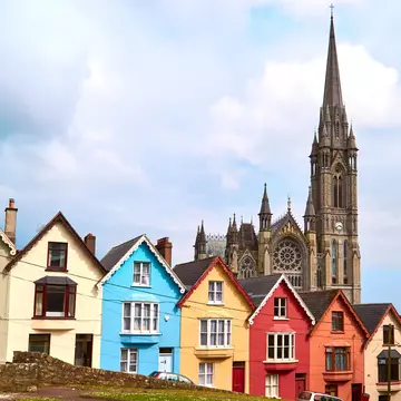 A stone cathedral is behind a row of brightly colored houses.