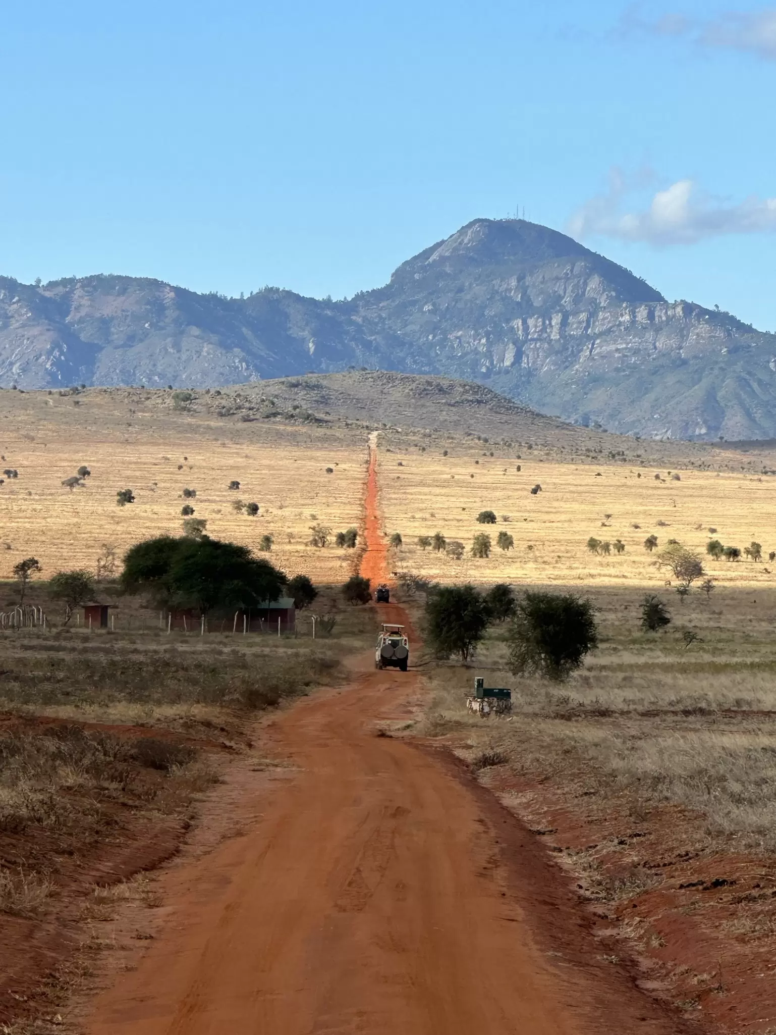 A vehicle on a red dirt road heading toward a mountain.