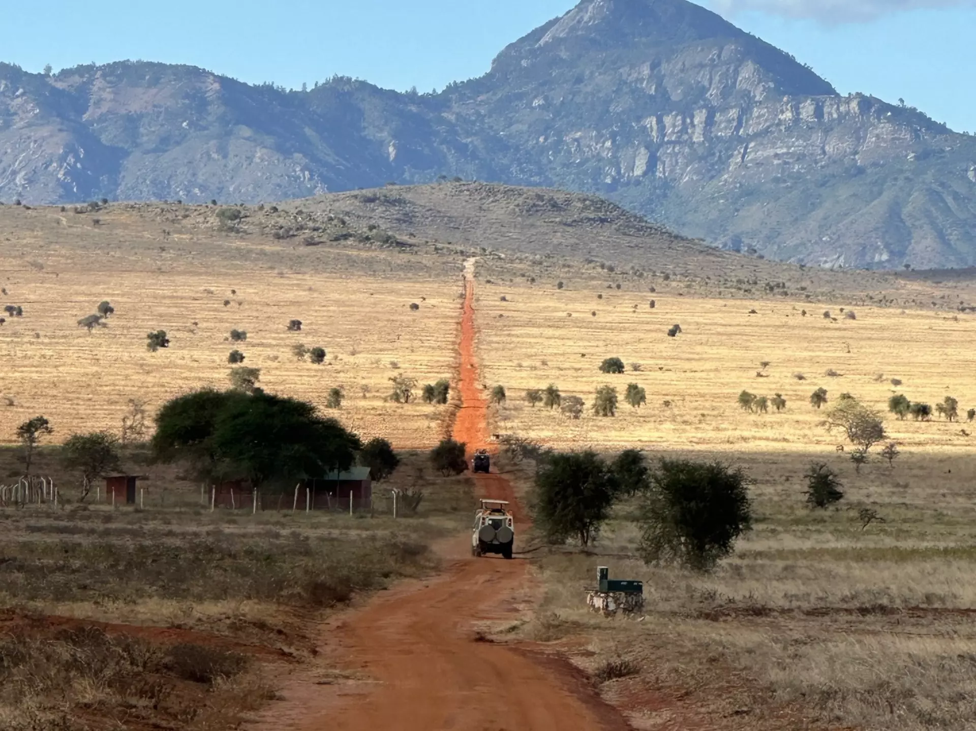 A vehicle on a red dirt road heading toward a mountain.