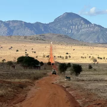 A vehicle on a red dirt road heading toward a mountain.