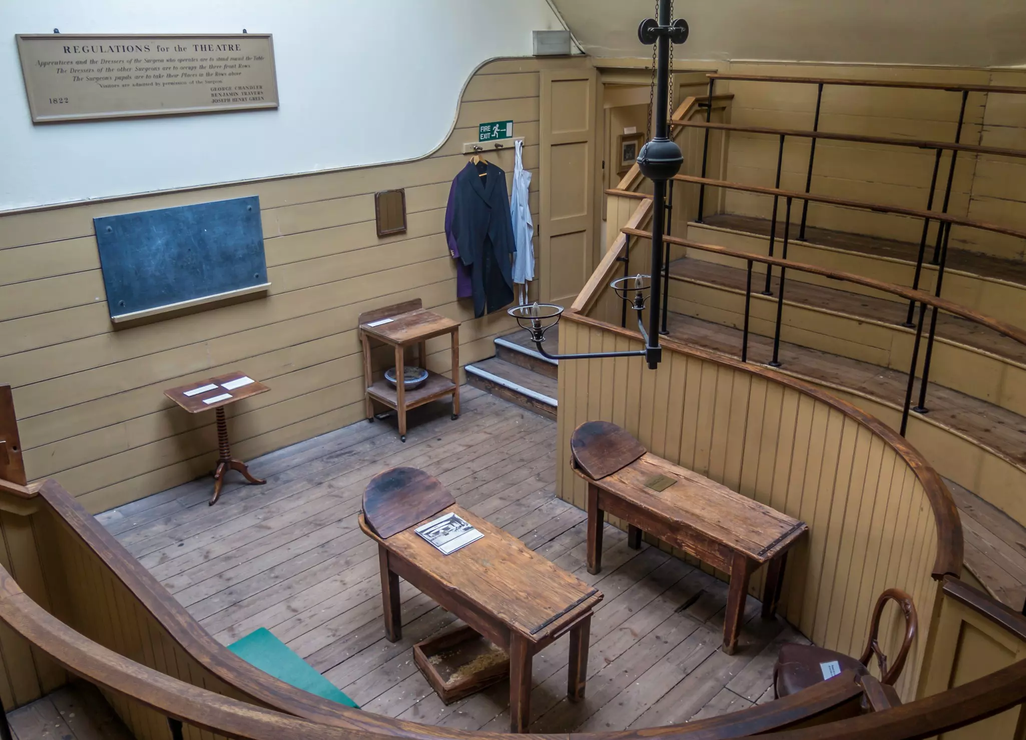 A wood-panelled room with a tiered viewing gallery around the sides. Two wooden operating tables are in the center of the room.