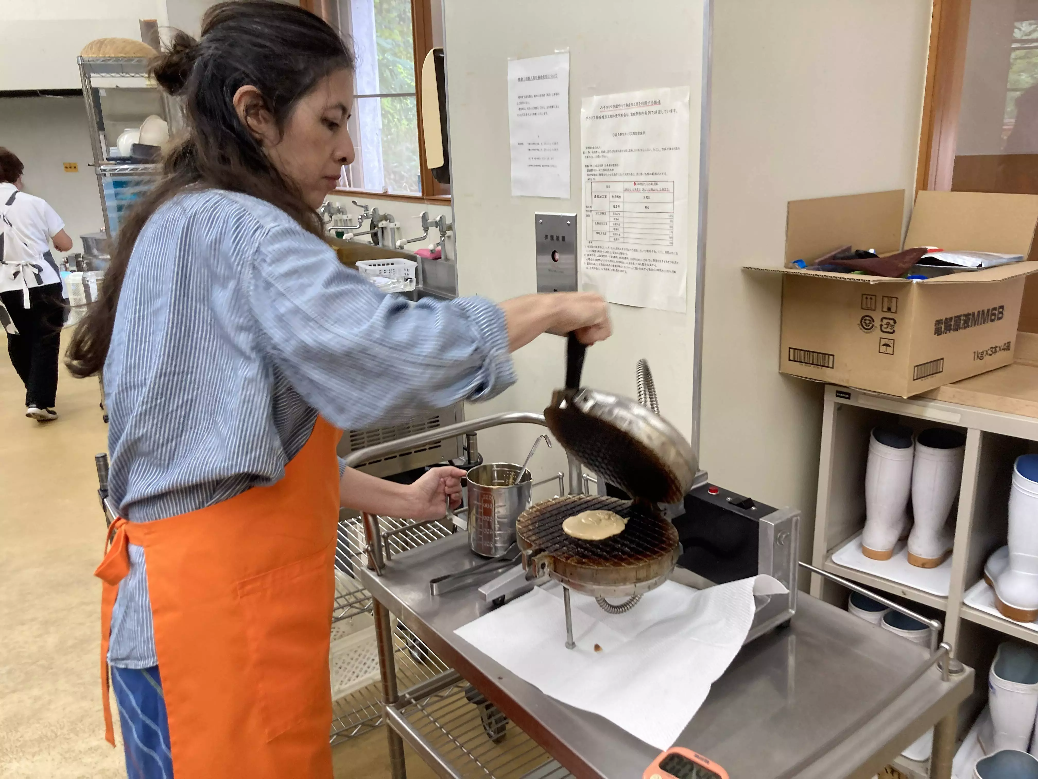 A woman wearing an orange apron operates a griddle during a workshop in a working dairy.