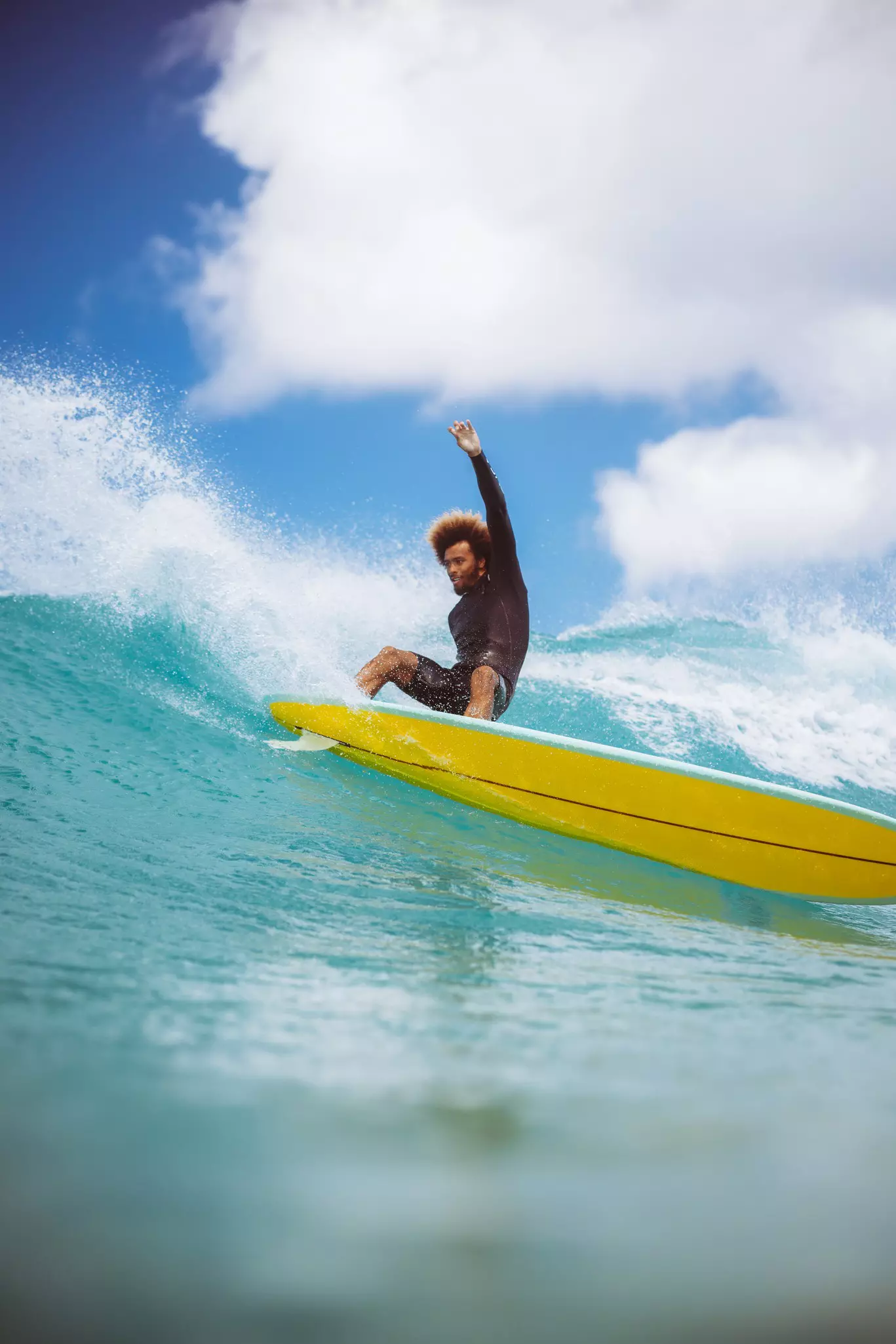 A surfer in a black wetsuit slides down a green wave with the sun behind it in Mexico