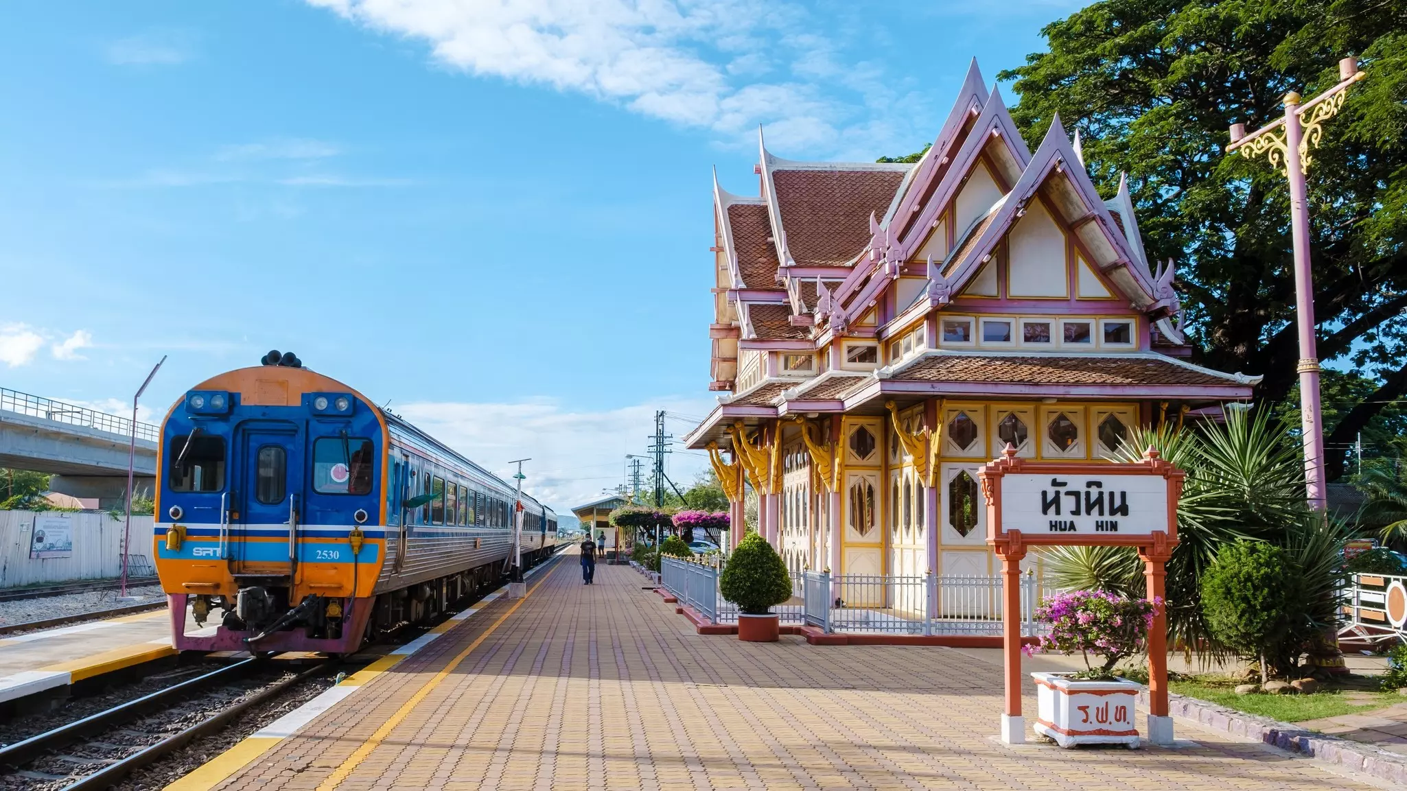 A train sits at a platform at a station. The station house is elaborately decorated with red and white paint and wooden details.