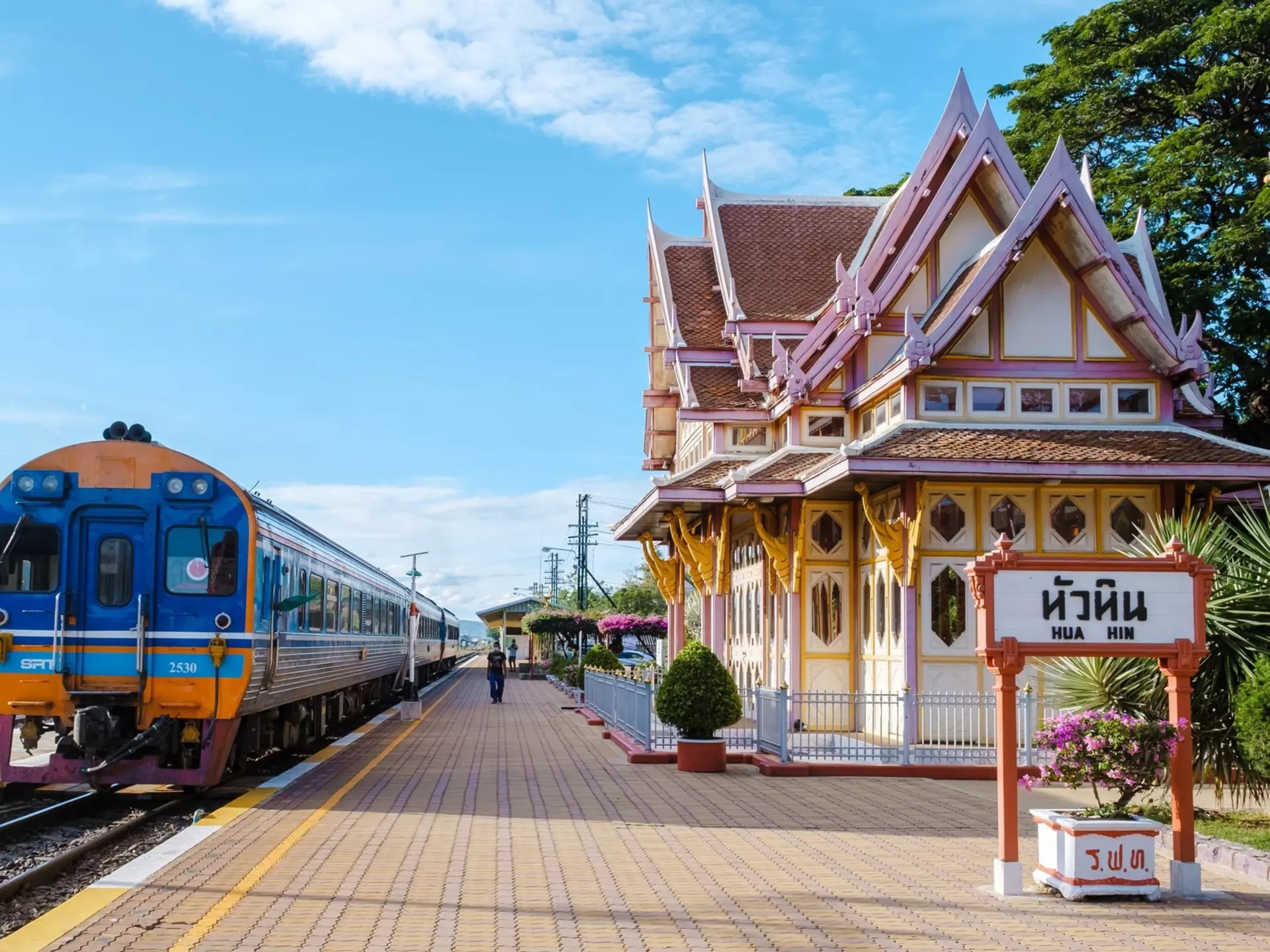 A train sits at a platform at a station. The station house is elaborately decorated with red and white paint and wooden details.