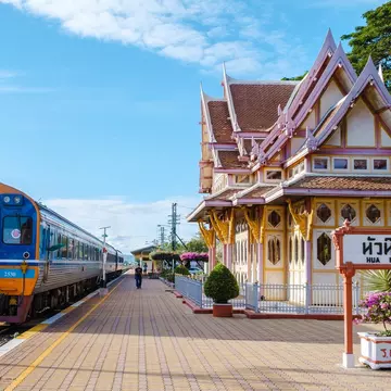 A train sits at a platform at a station. The station house is elaborately decorated with red and white paint and wooden details.