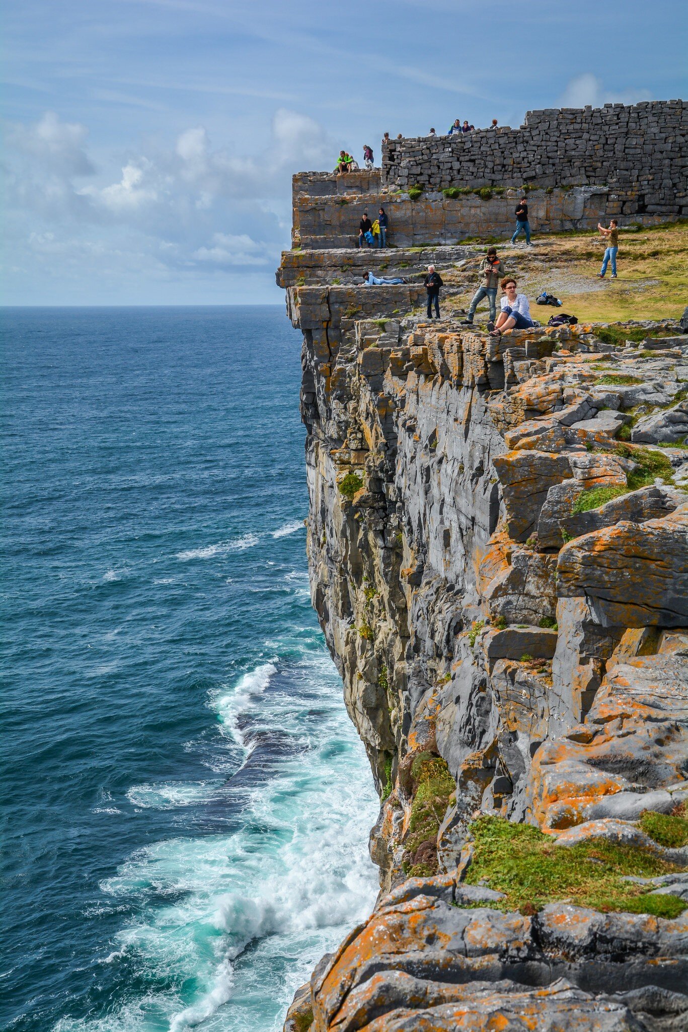 Visitors at the edge of a sheer cliff below the drystone ramparts of Dun Aengus