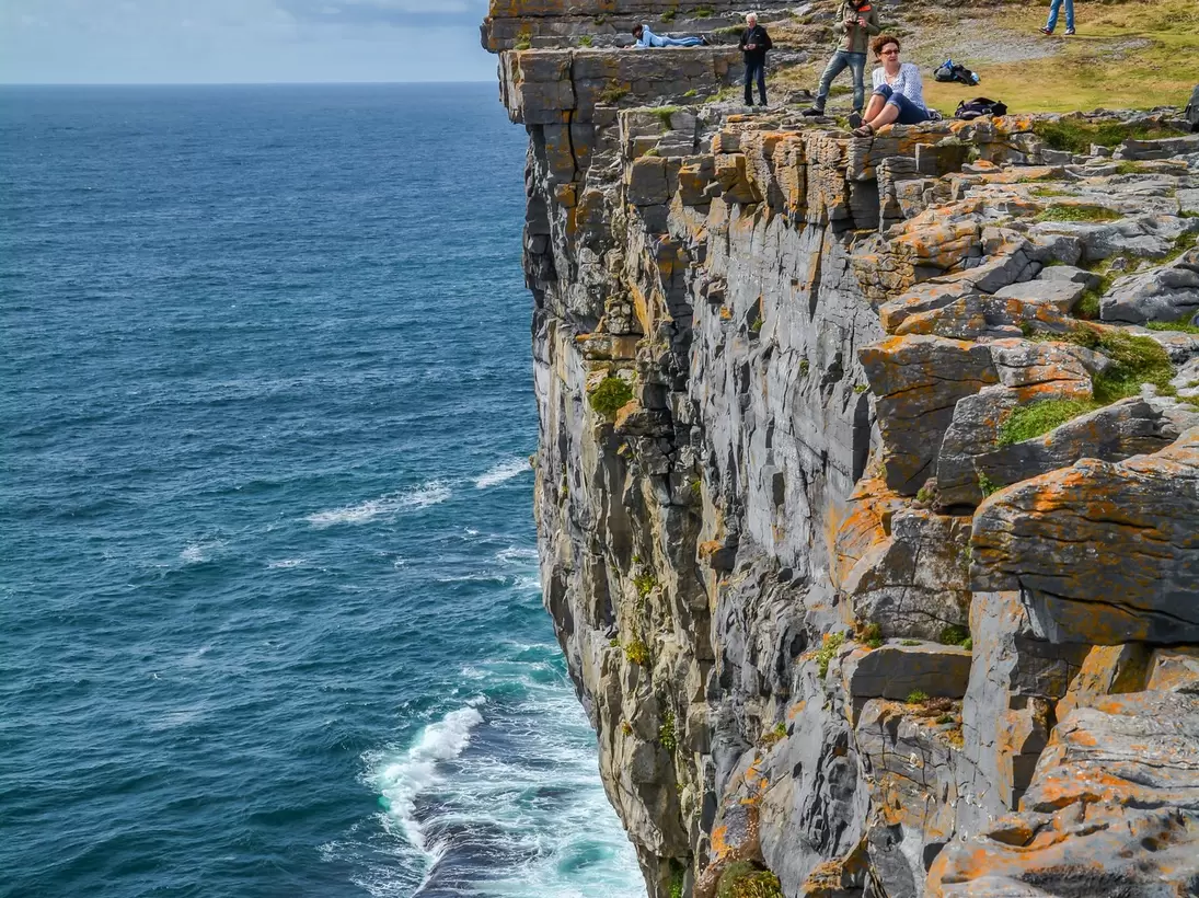 Visitors at the edge of a sheer cliff below the drystone ramparts of Dun Aengus