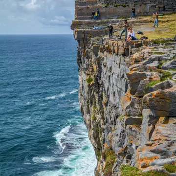 Visitors at the edge of a sheer cliff below the drystone ramparts of Dun Aengus