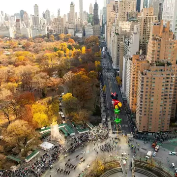 City streets and a vast park stretch out below in a view from a high-rise hotel. Large cartoon-character balloons are carried down the street in a parade. Views of The Macy’s Thanksgiving Day Parade from above. Mandarin Oriental, New York