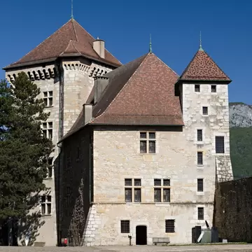 Stone towers with steep red-tiled roofs around the courtyard of Château d'Annecy, with a forested ridge behind.