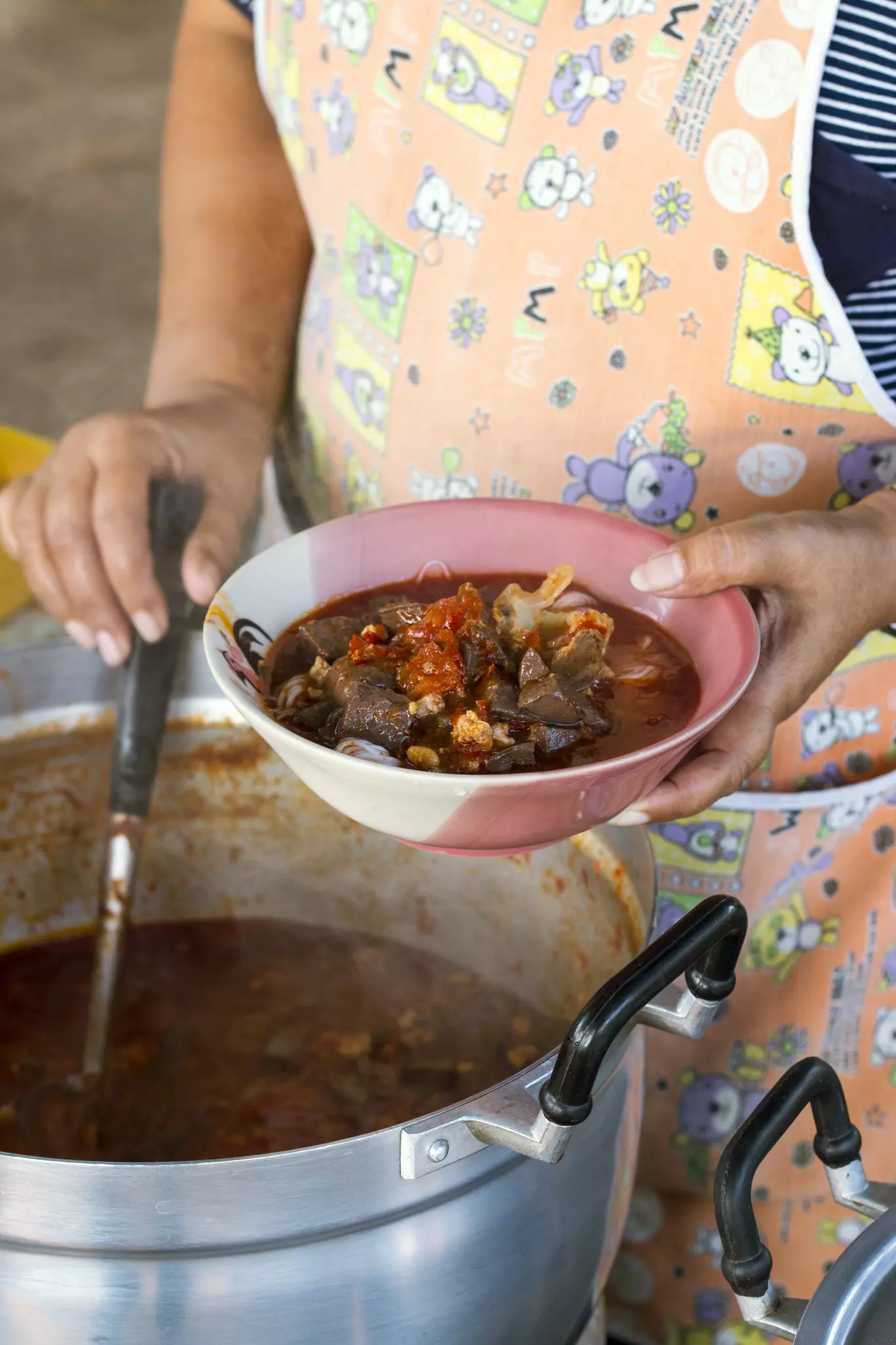 A lady pours soup from a ladle at a market