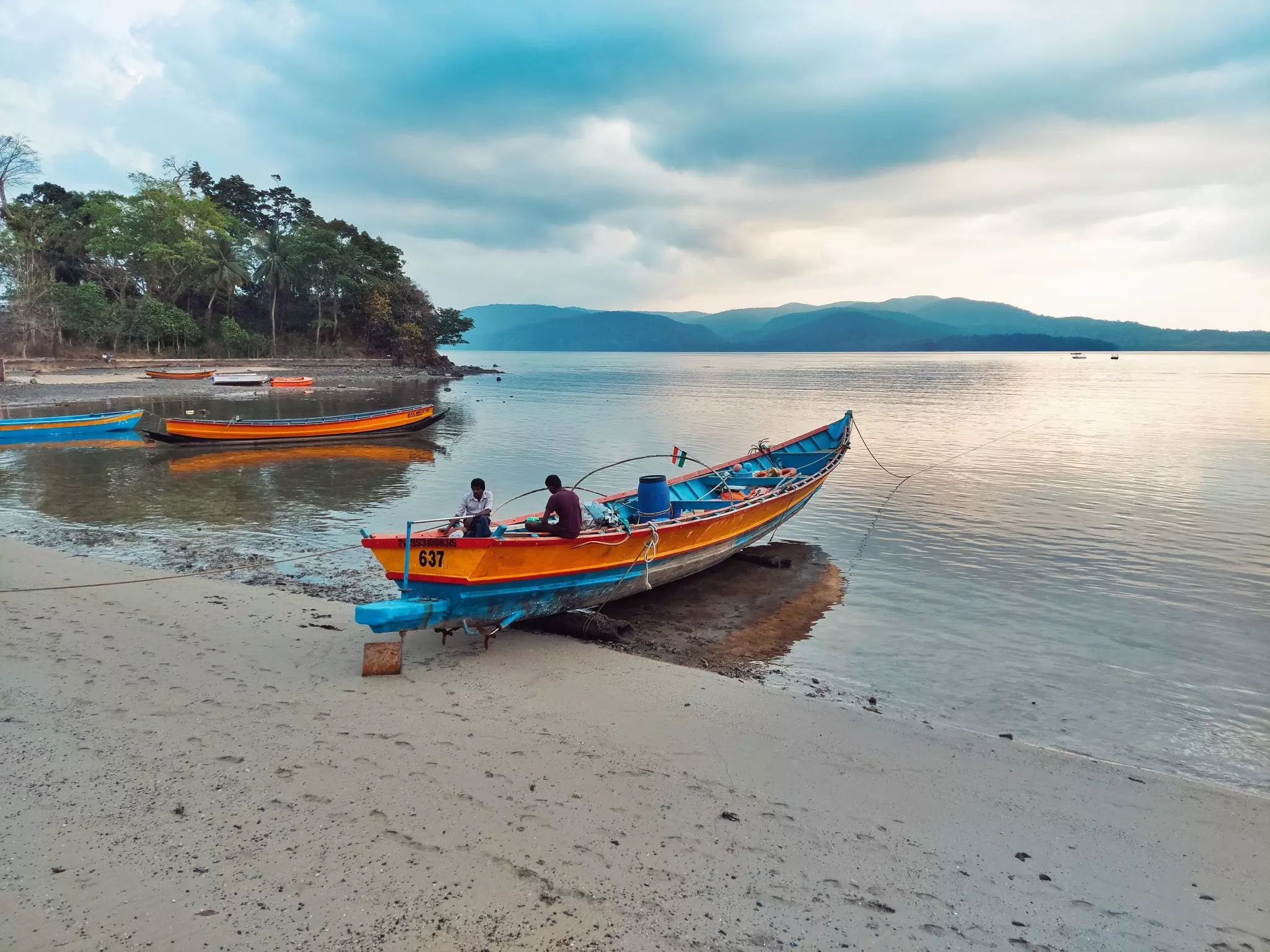 A brightly painted fishing boat is pulled up on the sand at a beach on a tropical island.
