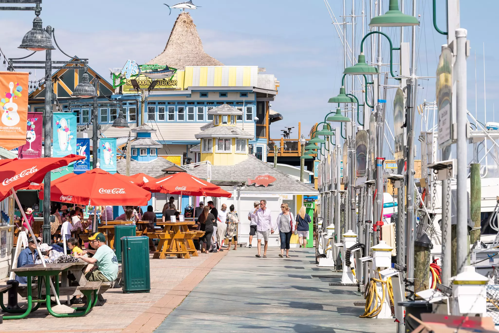 HarborWalk Village with boardwalk at marina, people sitting eating outside at restaurant cafe on summer day in Florida Panhandle, Gulf of Mexico