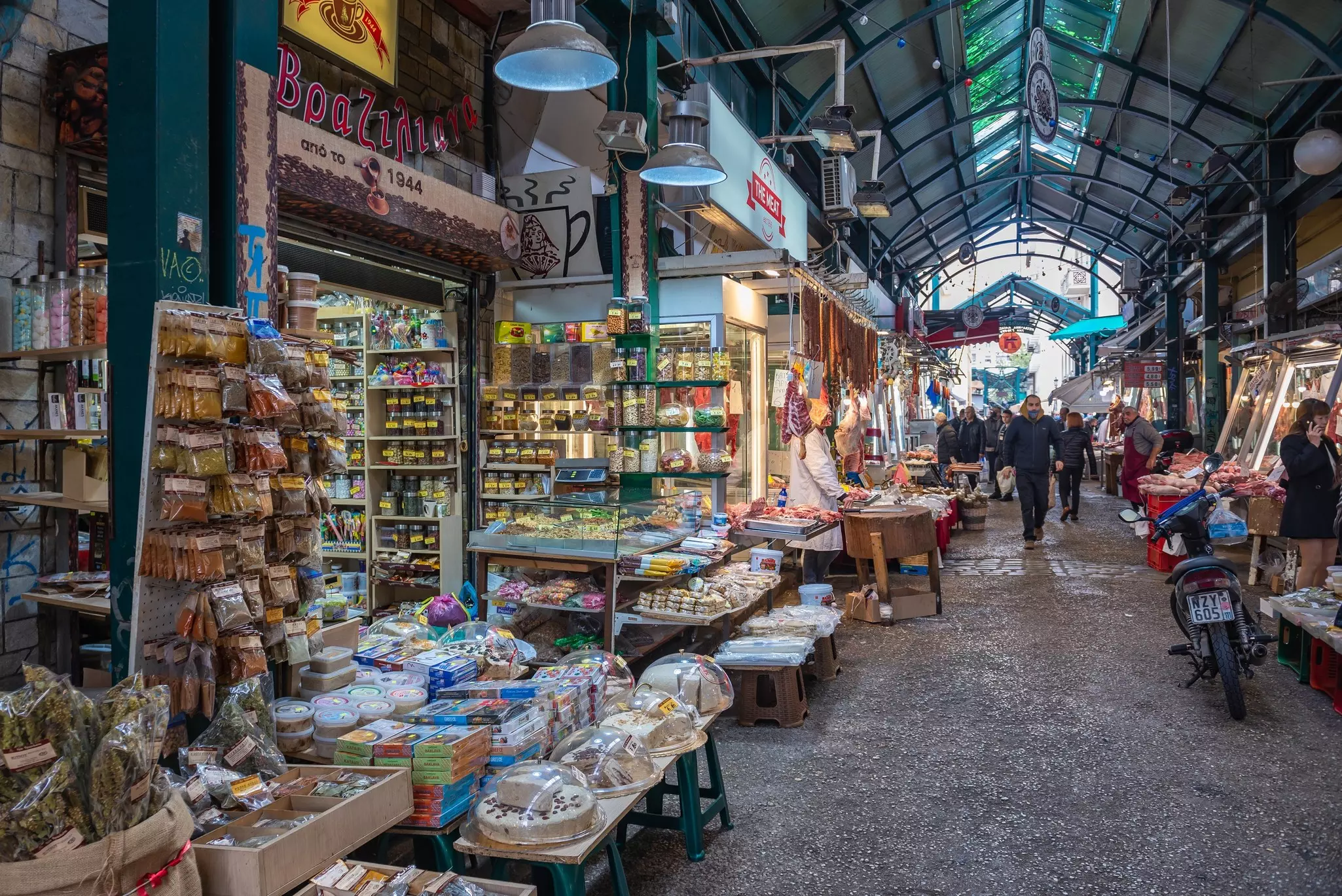 People walking down the aisle of tightly packed food stalls in an open-air market
