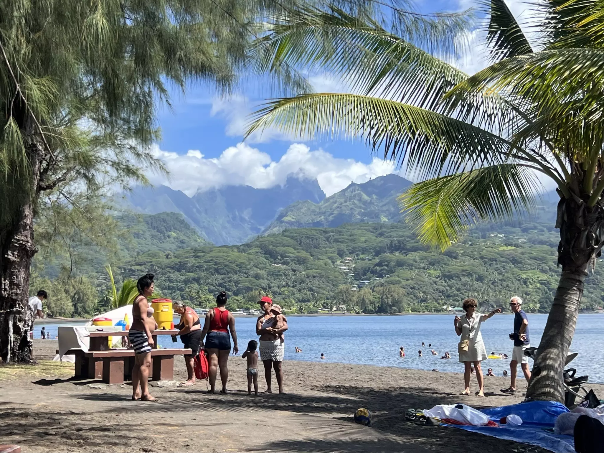 People in the water and on the black sand beach at Tahiti's Pointe Vénus