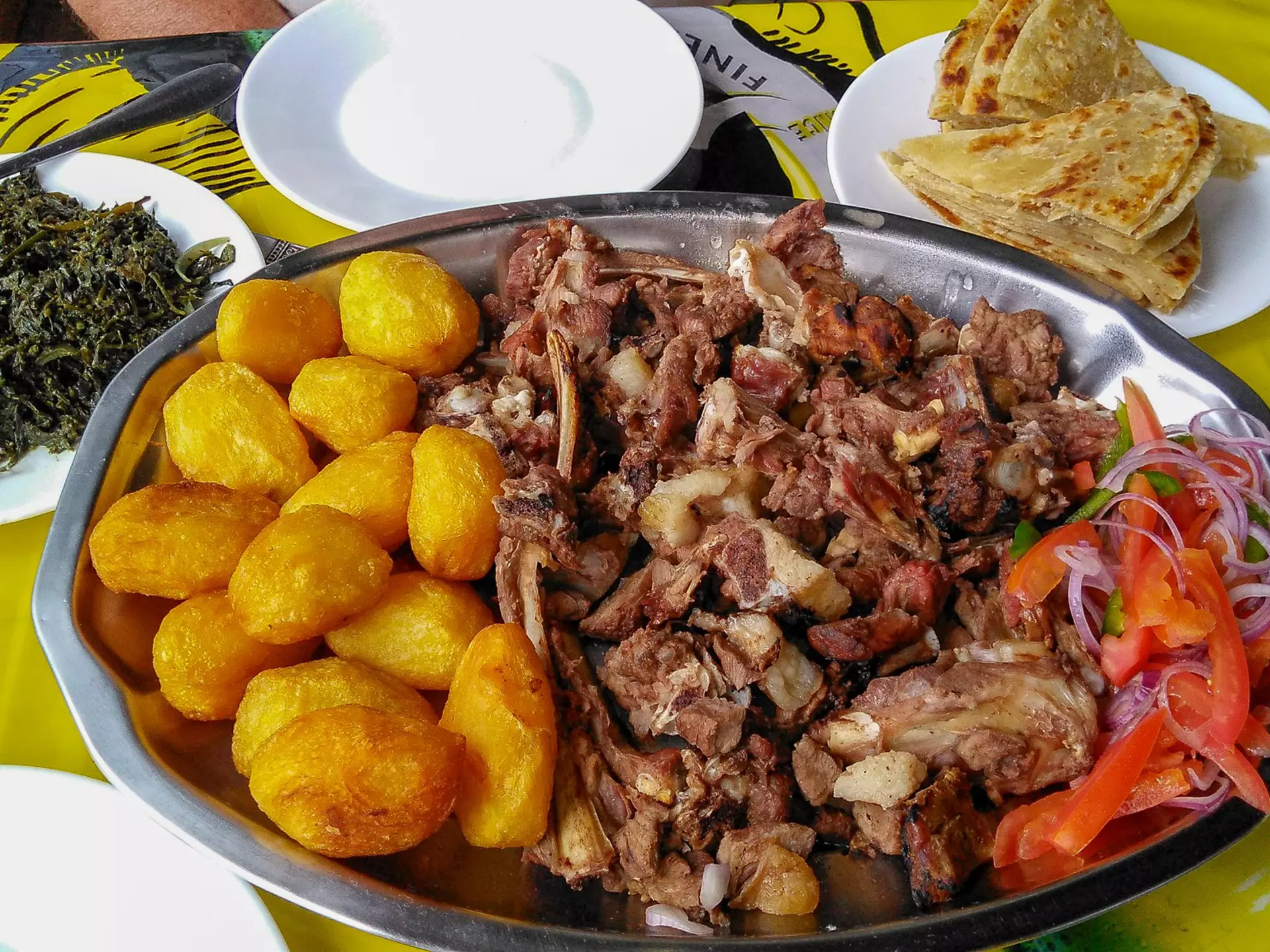 Sharing platter of a traditional Kenyan dish, Nyama choma and accompaniments of kachumbari salad, sukuma wiki, chapati and roast potatoes.