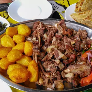 Sharing platter of a traditional Kenyan dish, Nyama choma and accompaniments of kachumbari salad, sukuma wiki, chapati and roast potatoes.