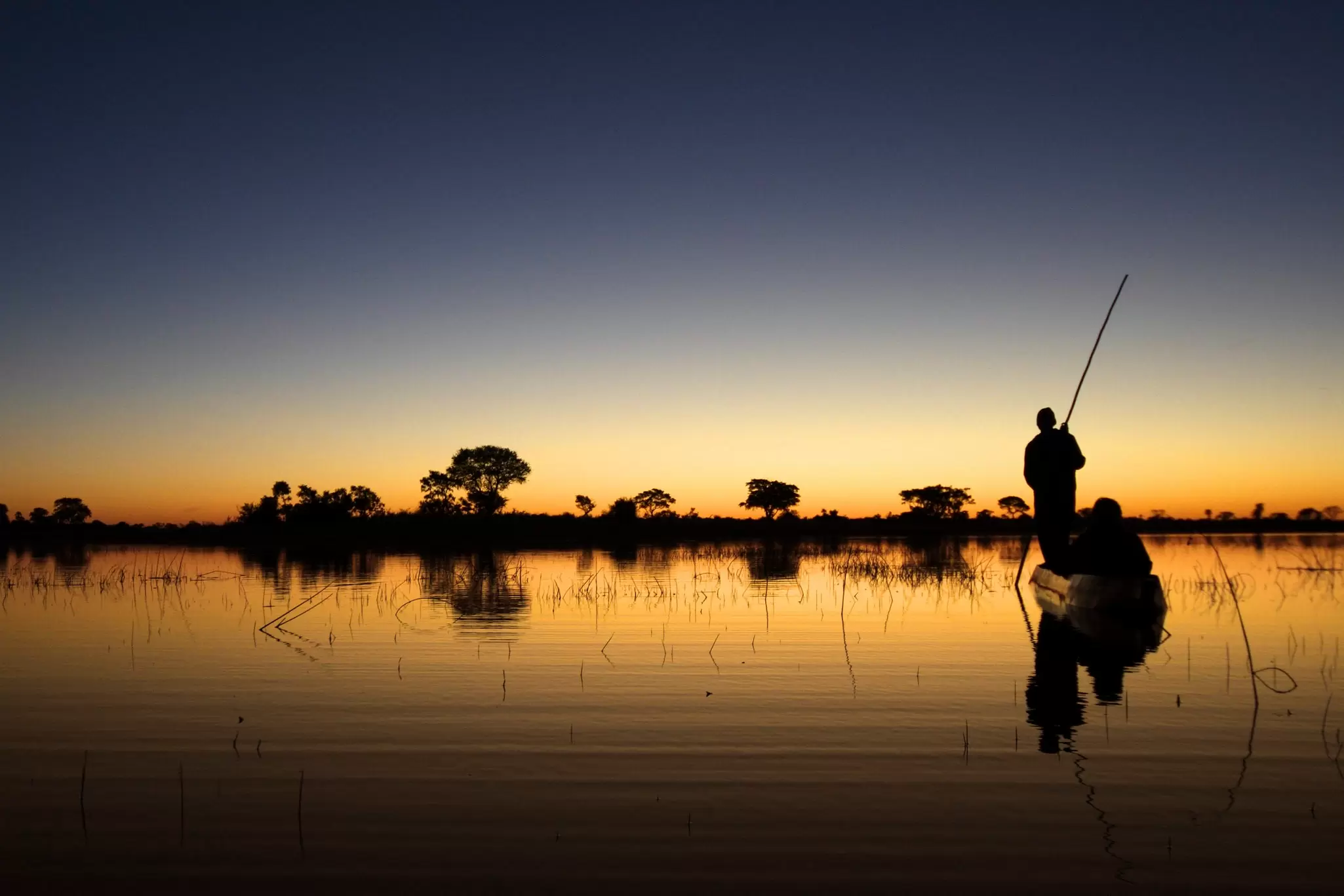 A small wooden canoe being paddled through a waterway at sunset: The Okavango Delta in Botswana