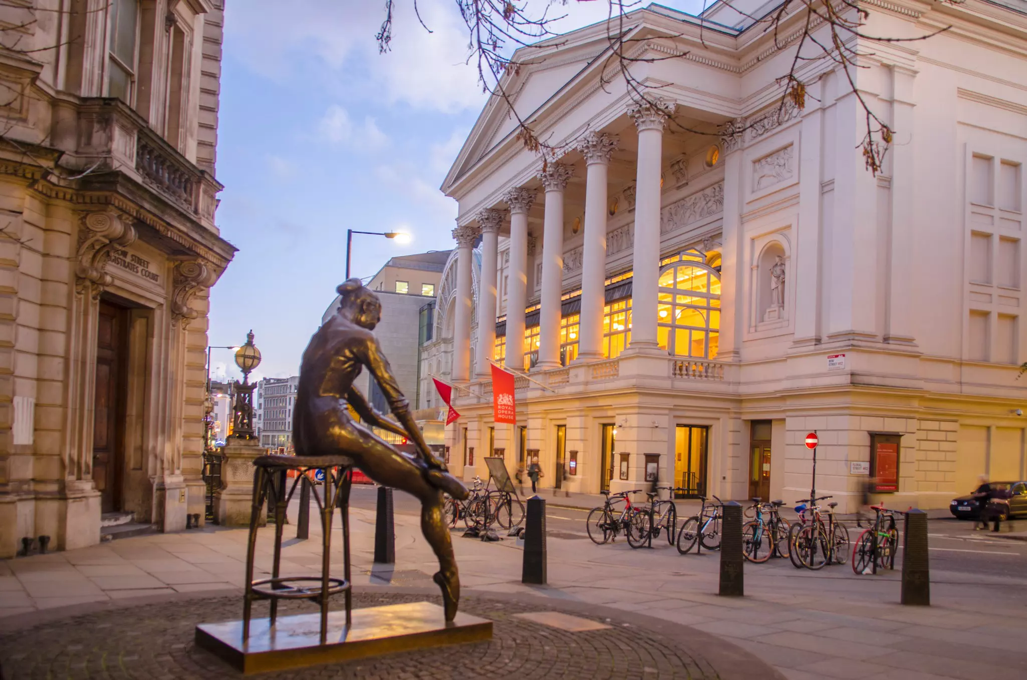  A bronze statue of a ballerina stands outside a ballet and opera venue at dusk.