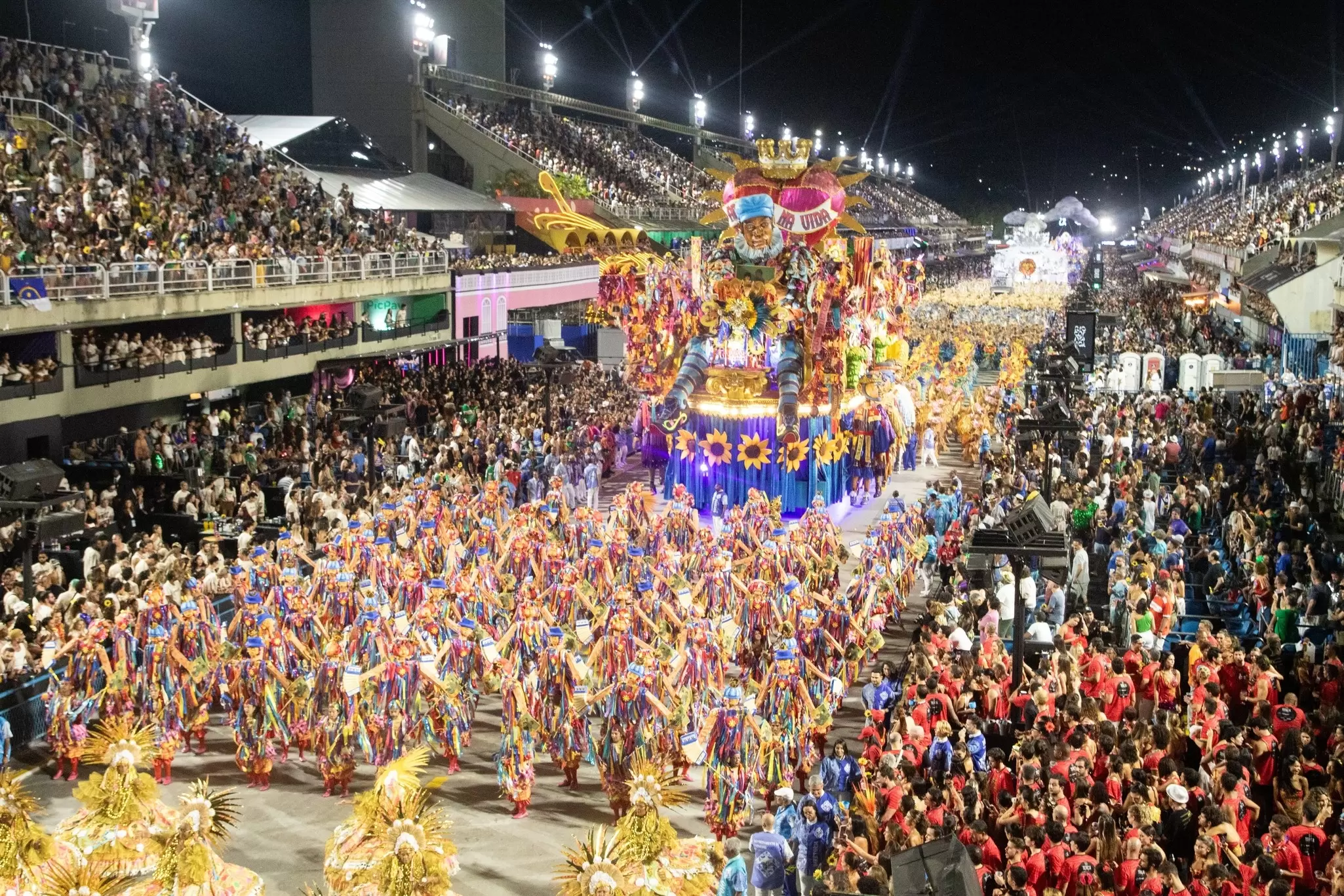 Dancers in costume lead a float through stands of onlookers.