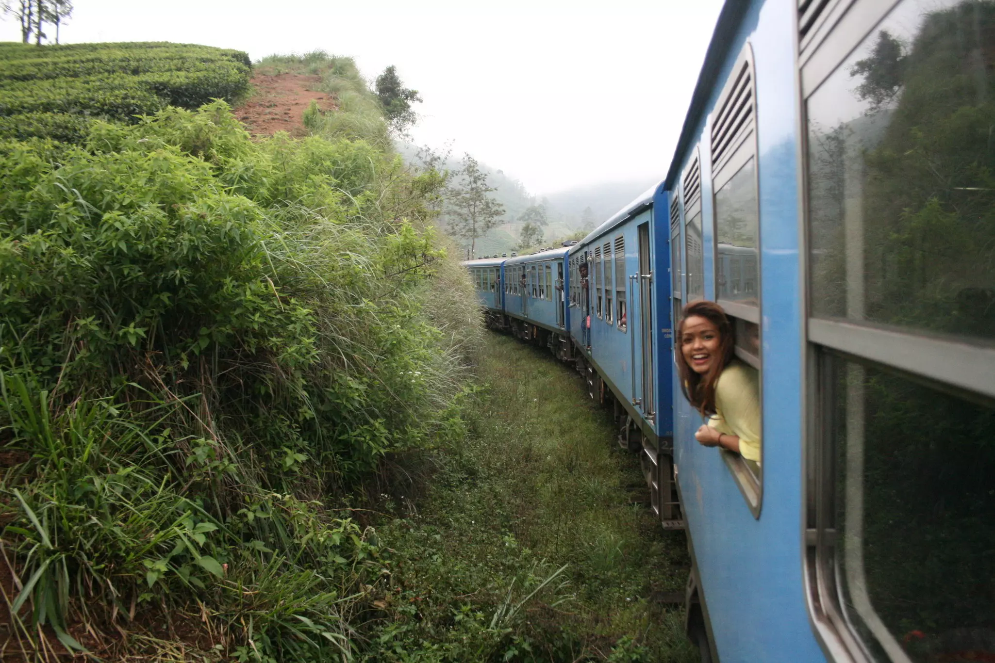 An backpacker leans out the window of the Blue Train from Kandy to Ella in the Sri Lankan mountains
