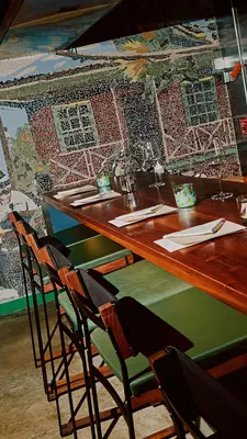 Green and wood bar stools are tucked under a wooden bar set with napkins. 