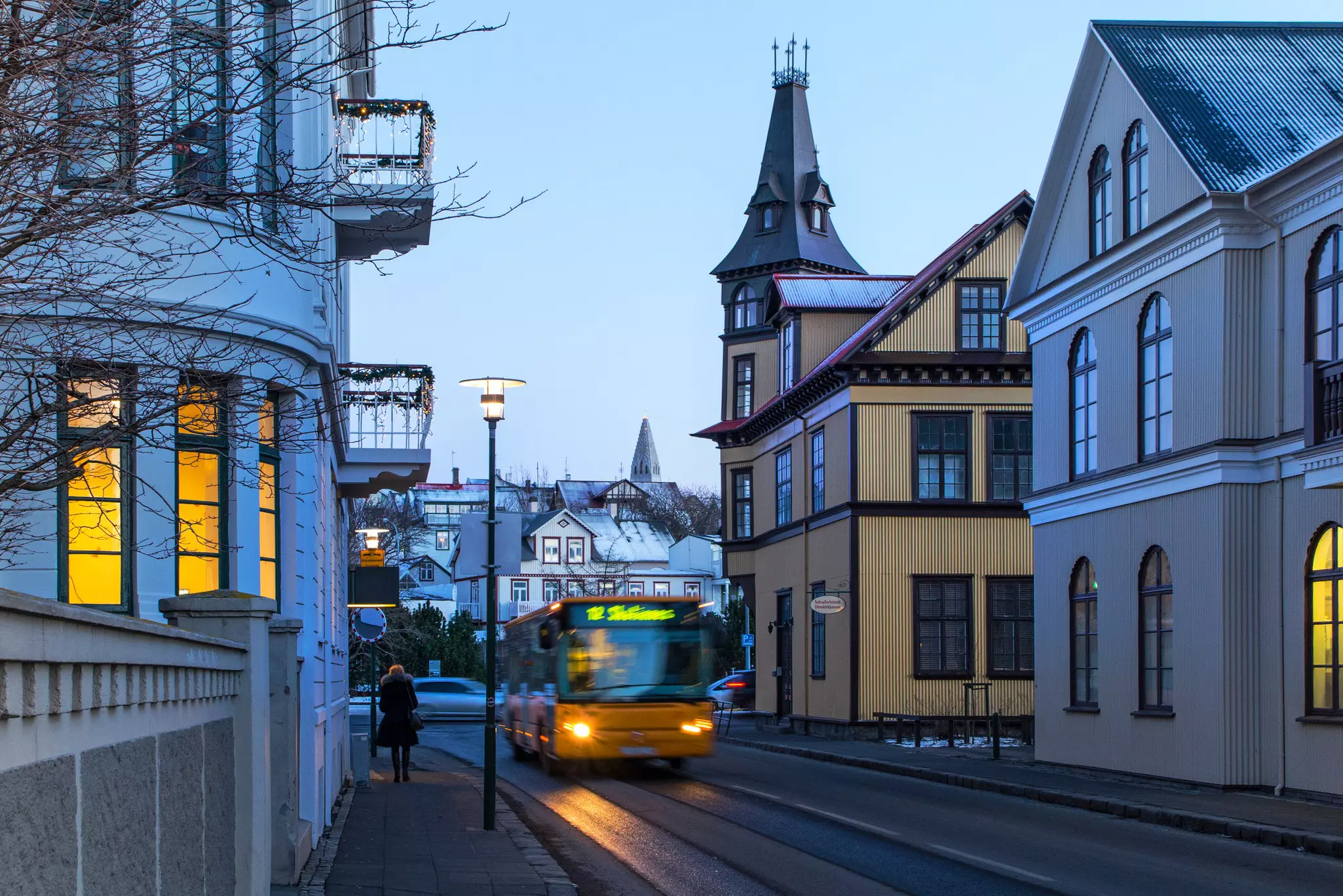 The headlights a bus navigating a city street are seen at dusk.