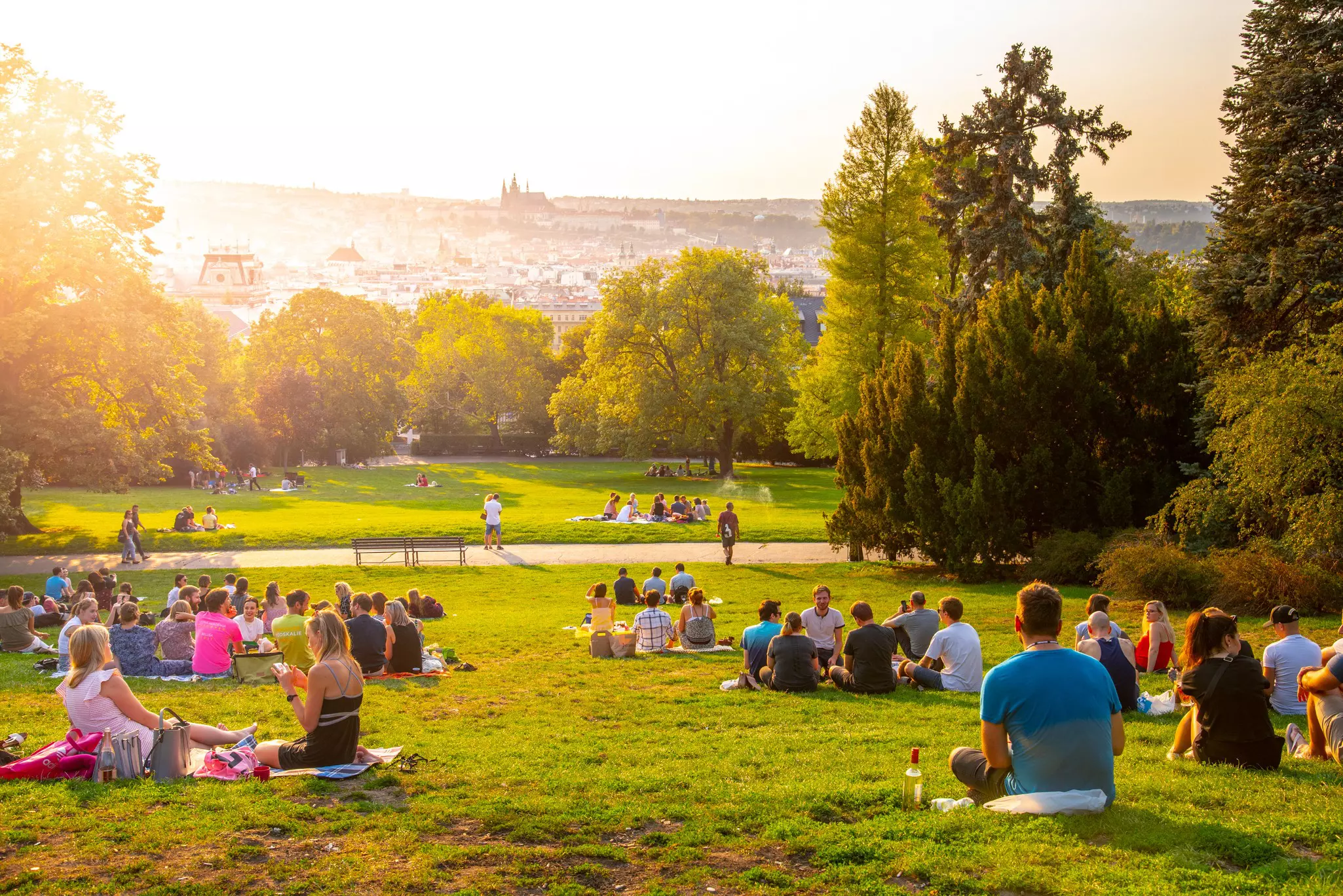 People sitting on grass and picnicking at sunset; there is an outline of a castle on the horizon.
