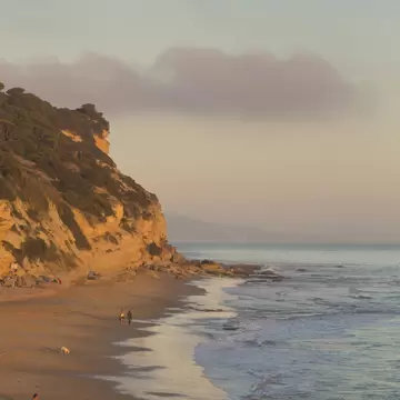 People walking along Playa de Los Caños during sunset on the Costa de la Luz in Spain.