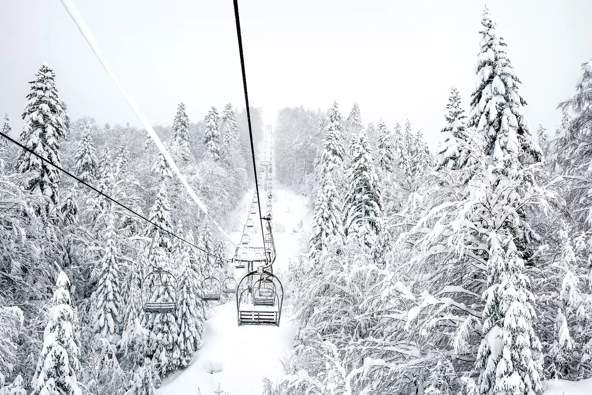 An empty ski lift through very snowy trees in Montenegro.