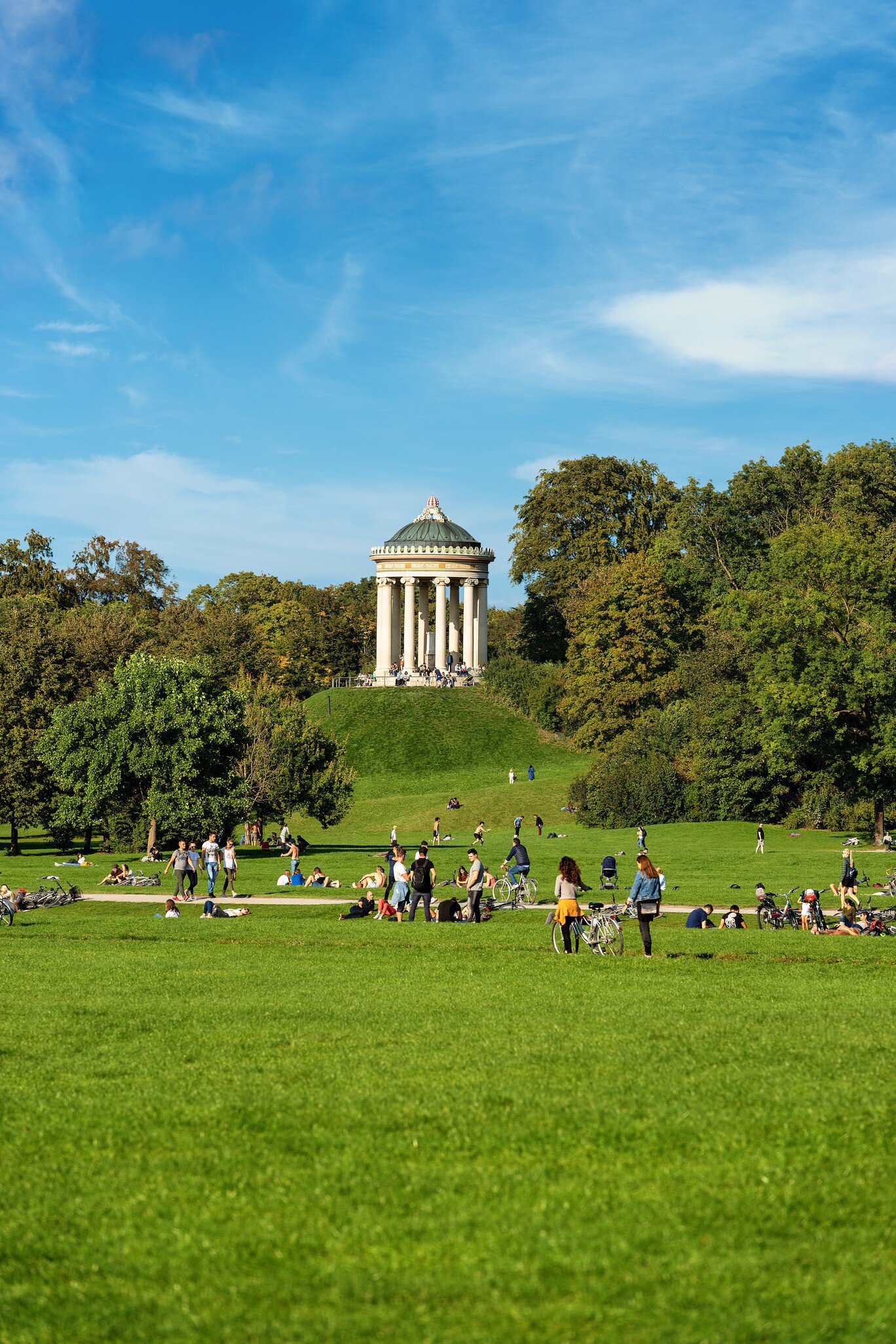 People spread out on the grass at Englischer Garten (English Garden) on a sunny day under the Monopteros temple.