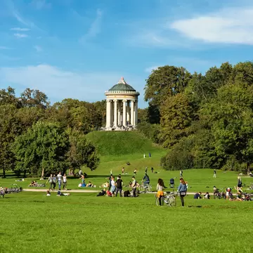 People spread out on the grass at Englischer Garten (English Garden) on a sunny day under the Monopteros temple.