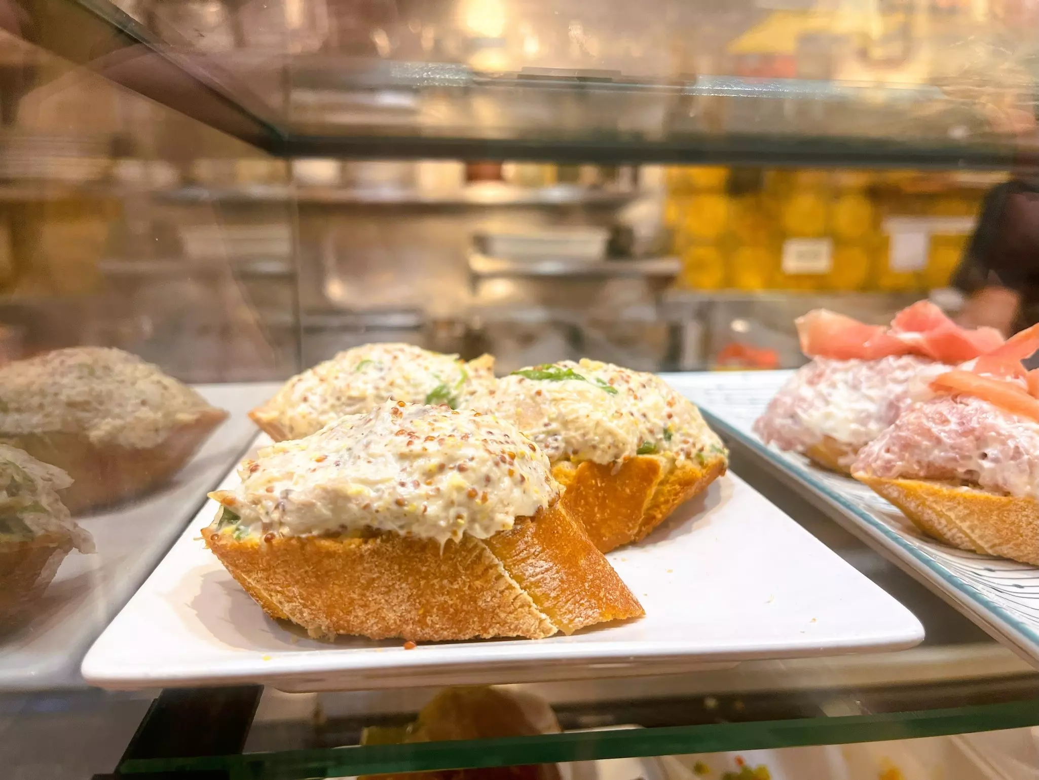 A slice of baguette with a paste on top on display at a counter in a bar.