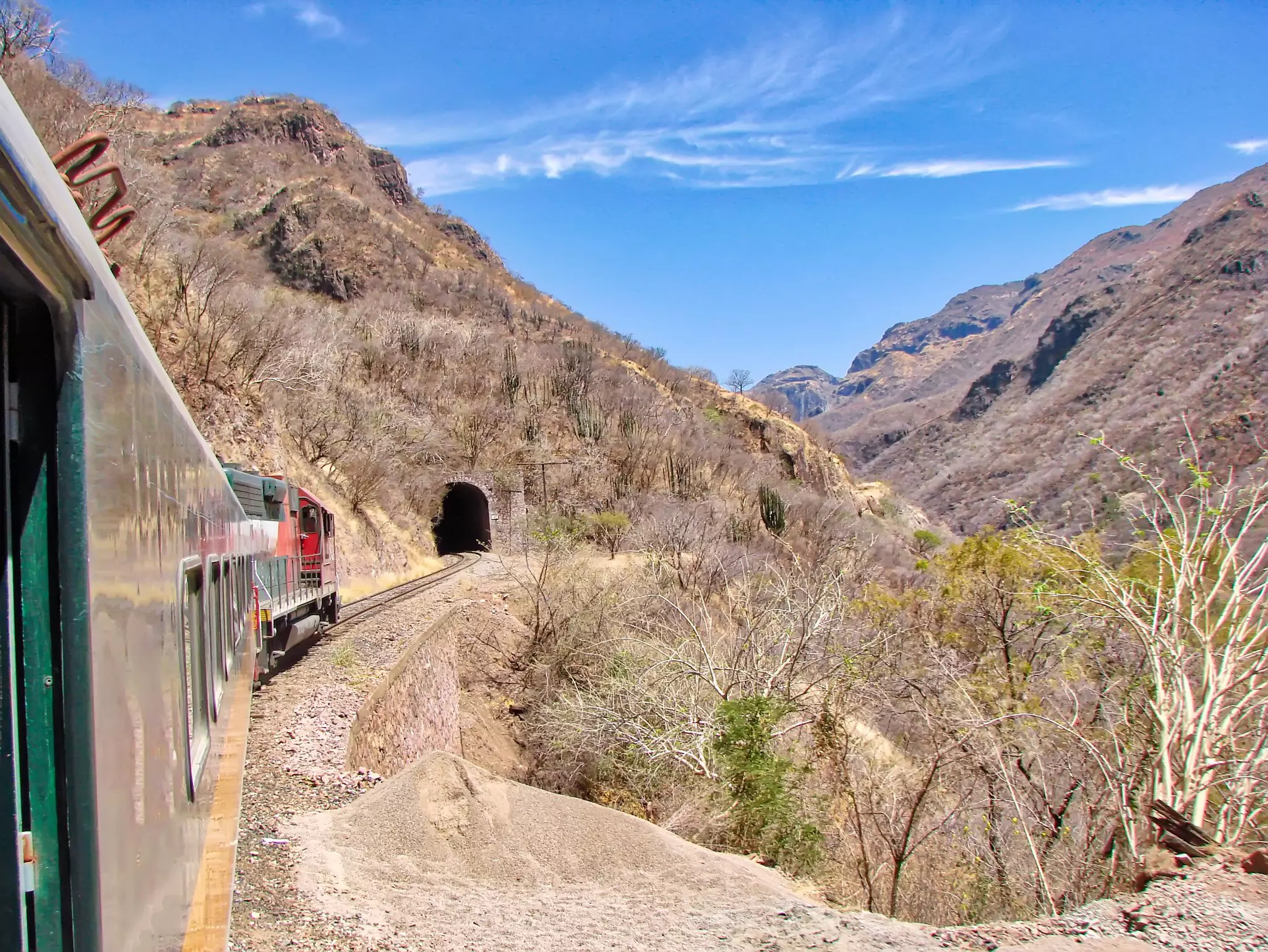 A train heads toward a tunnel in a desert mountain landscape.