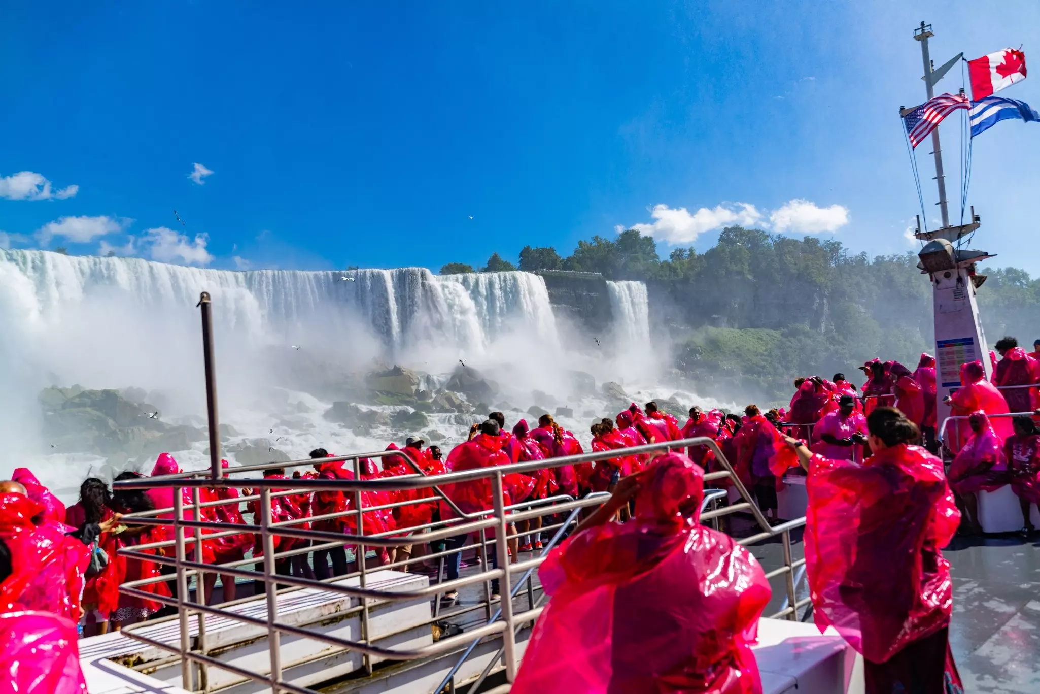 Beautiful Niagara Falls, on the famous Falls boat tour, the Canadian and American flag flying on the mast of Niagara Cruise Boat with tourist wearing rain jackets.