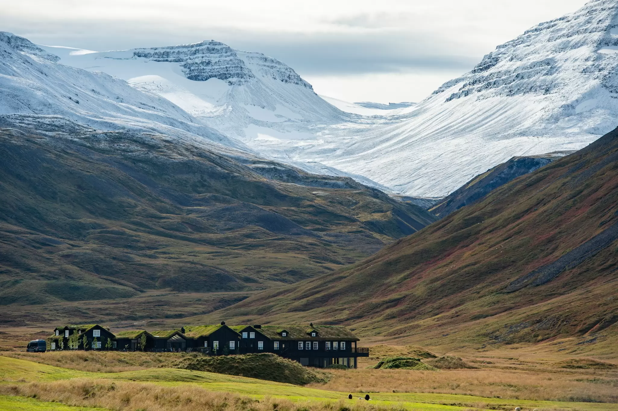 A series of wooden buildings tucked into the foot of a mountain range: Eleven Deplar Farm in Iceland.