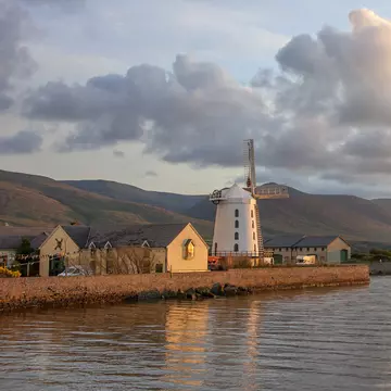 Blennerville Windmill, Blennerville (Tralee), Ireland. Historic tower mill from 1800, now a tourist attraction. Wide view at sunset with windmill, cloudy sky, and water.