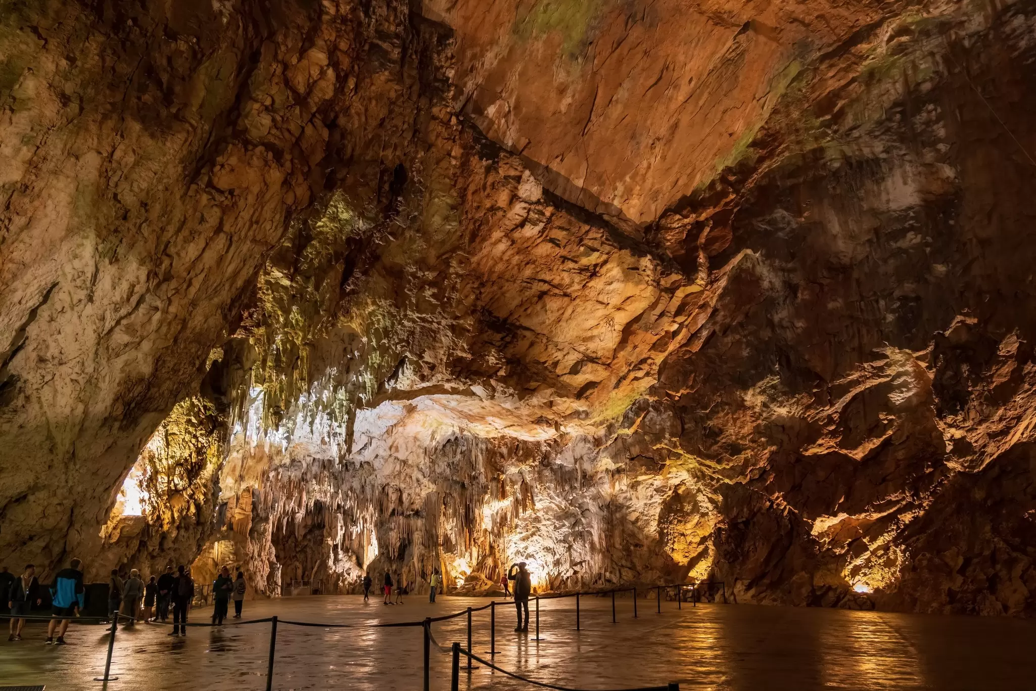 A large underground cavern illuminated by several lights as tourists take pictures.